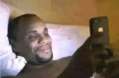 Homme souriant regardant son téléphone dans son lit la nuit