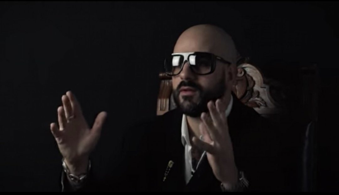 Papacito Homme chauve avec grosses lunettes noires en pleine explication dramatique – ambiance sérieuse, éclairage sombre, style mafia ou interview intense