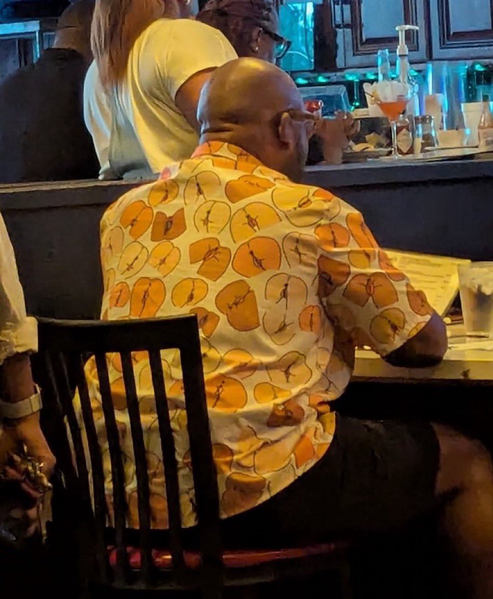 Homme portant une chemise à motifs de fesses vagin stylisées dans un restaurant – scène cocasse et inattendue