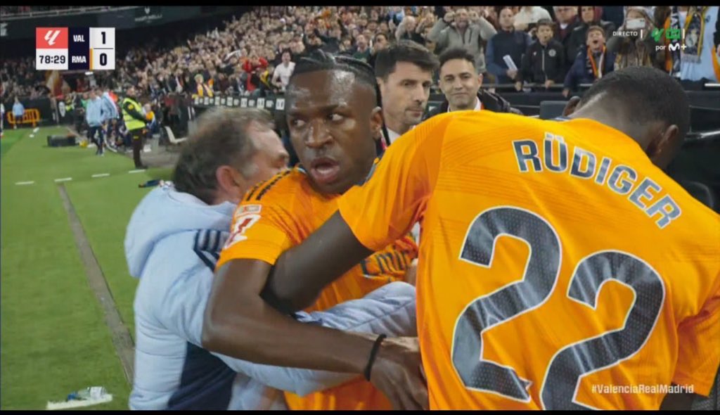 Vinícius Jr. retenu par Rüdiger et un membre du staff alors qu’il réagit à une provocation depuis les tribunes, lors du match tendu entre Valence et le Real Madrid. Regard choqué chokbar