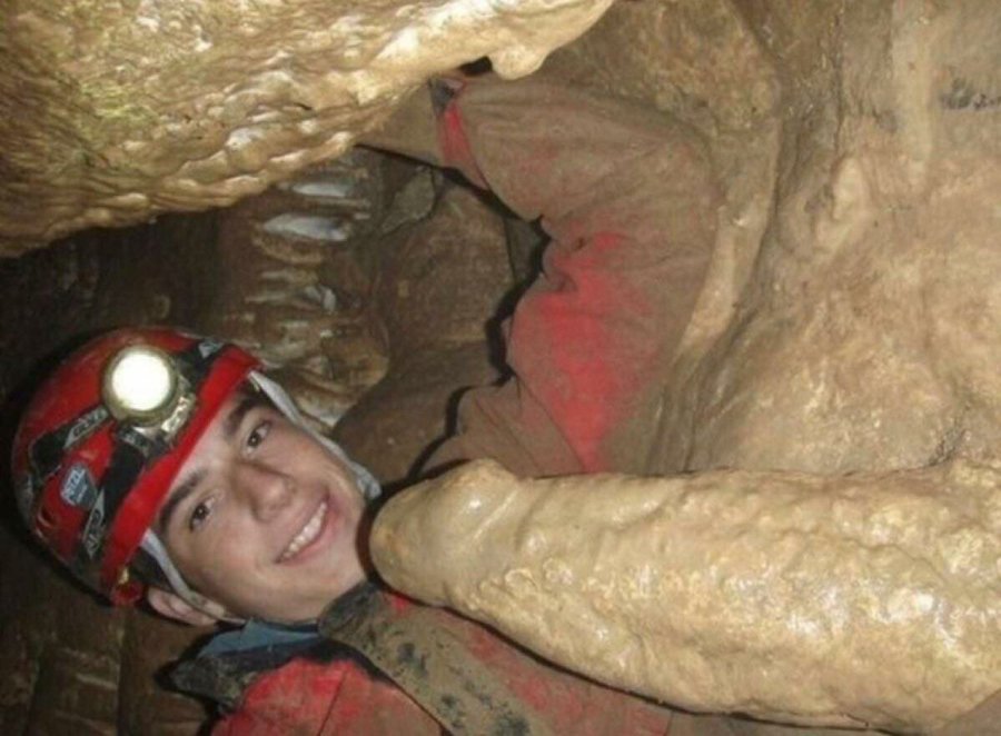 Un homme en exploration souterraine faisant face à une formation rocheuse ressemblant à une bite