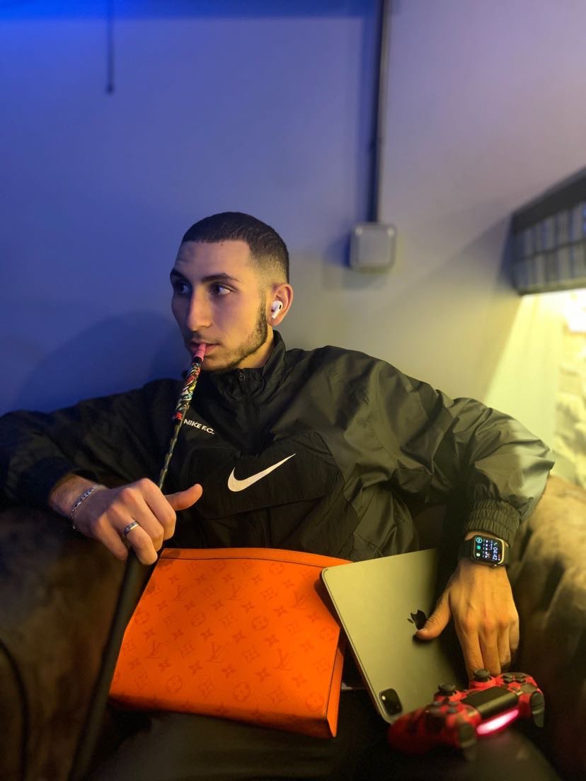 Homme qui flexe au max en fumant une chicha avec MacBook Airpods Apple Watch, Sacoche Louis Vuitton et manette PS5