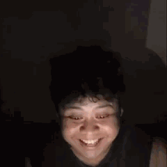 Un jeune homme ricane puis choqué face caméra dans le noir