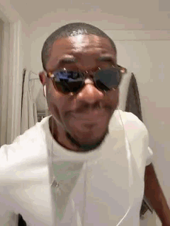 Un homme avec des lunettes de soleil dance et sourit devant sa caméra