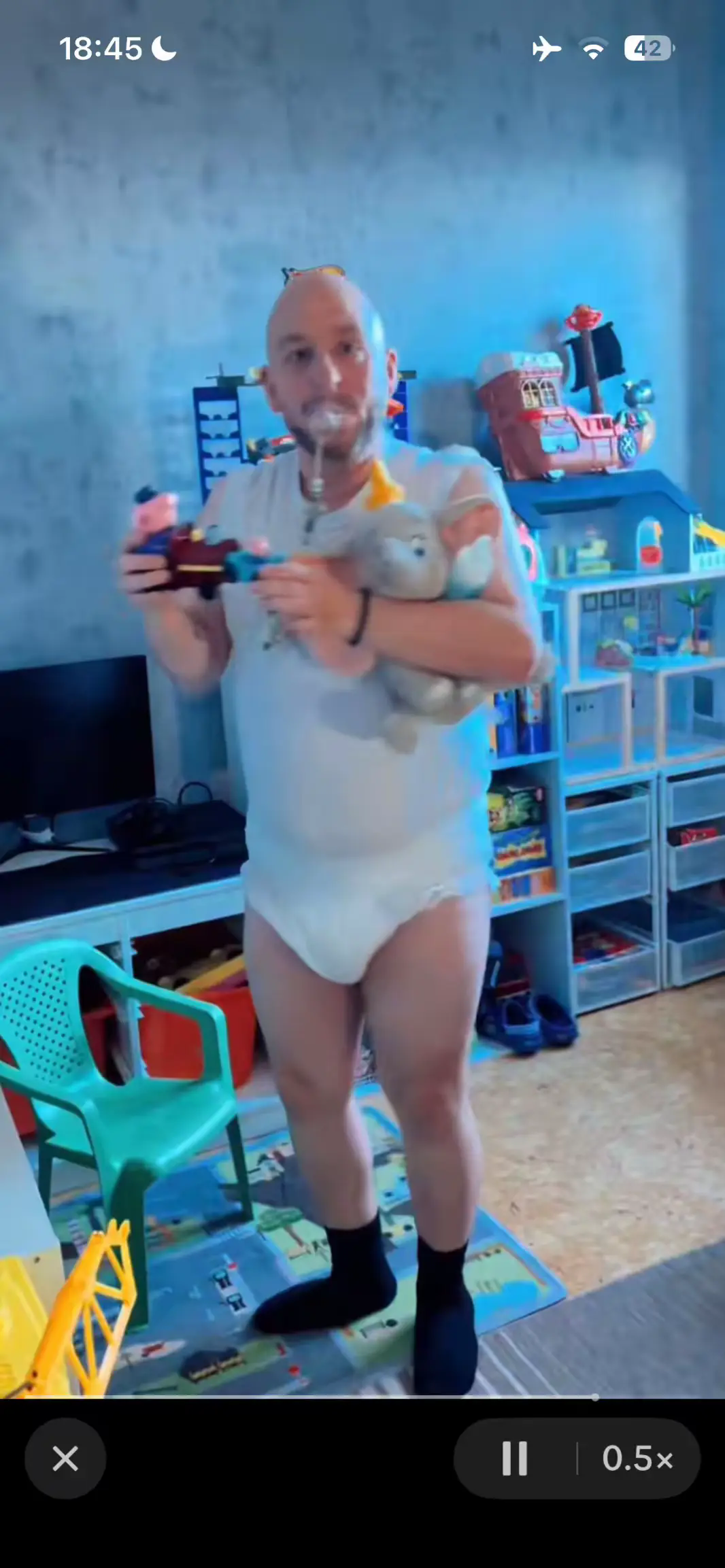 Un homme adulte habillé en bébé joue avec des jouets