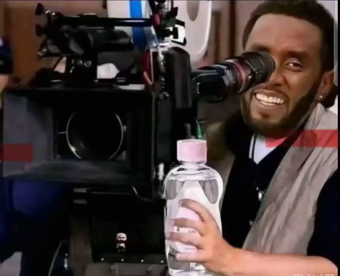P. Diddy sourit derrière une caméra avec une bouteille d'huile pour bébé