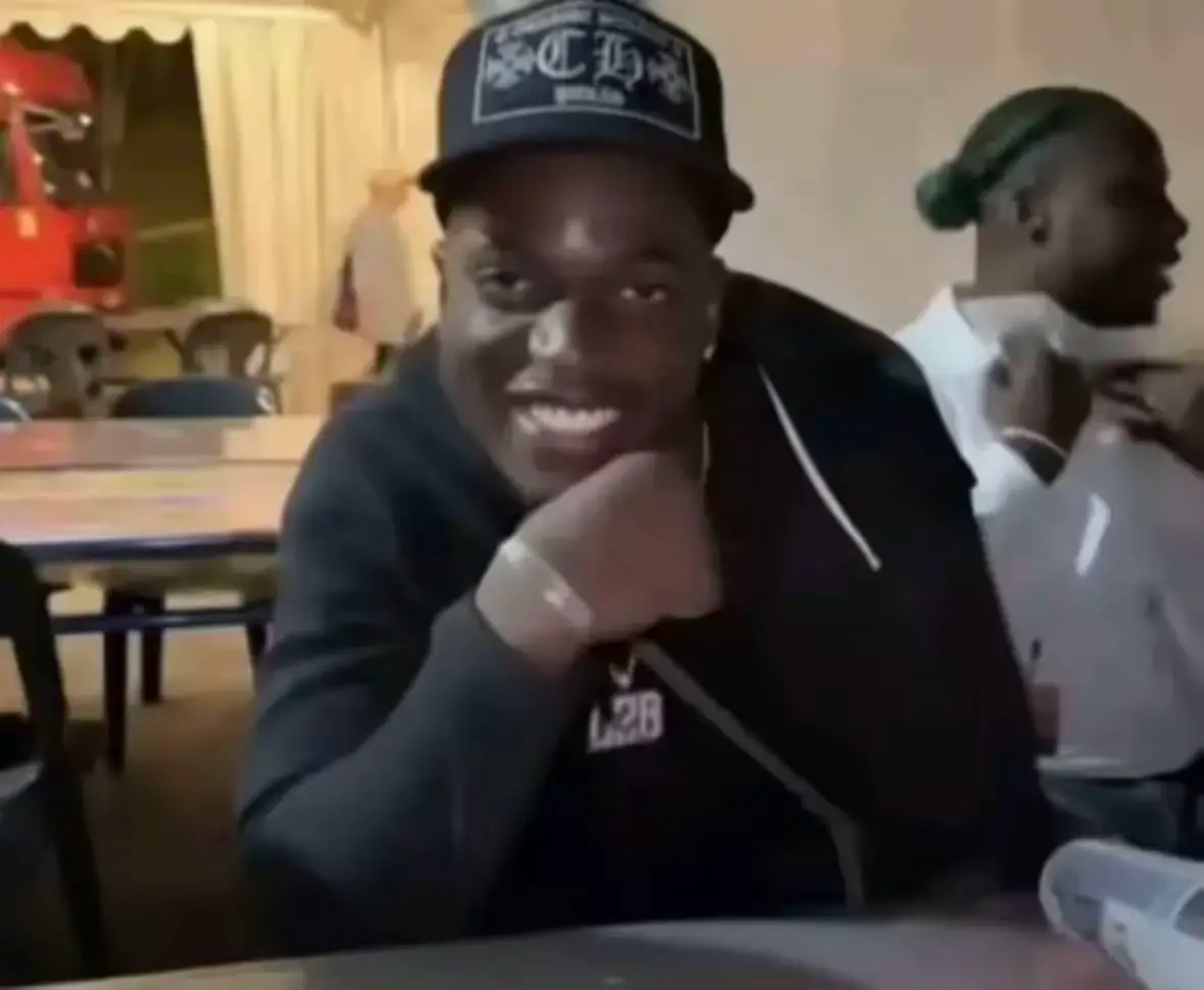 Un homme au casquette sourit malicieusement à la caméra