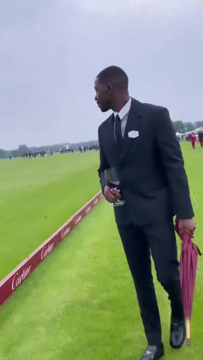 Un homme très classe marche sur une pelouse avec un verre de vin et un parapluie