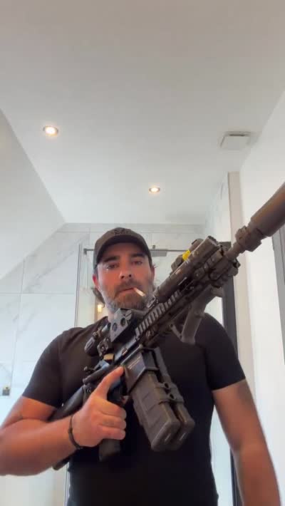 Akram Junior pose avec un fusil d'assaut et une cigarette dans sa salle de bain